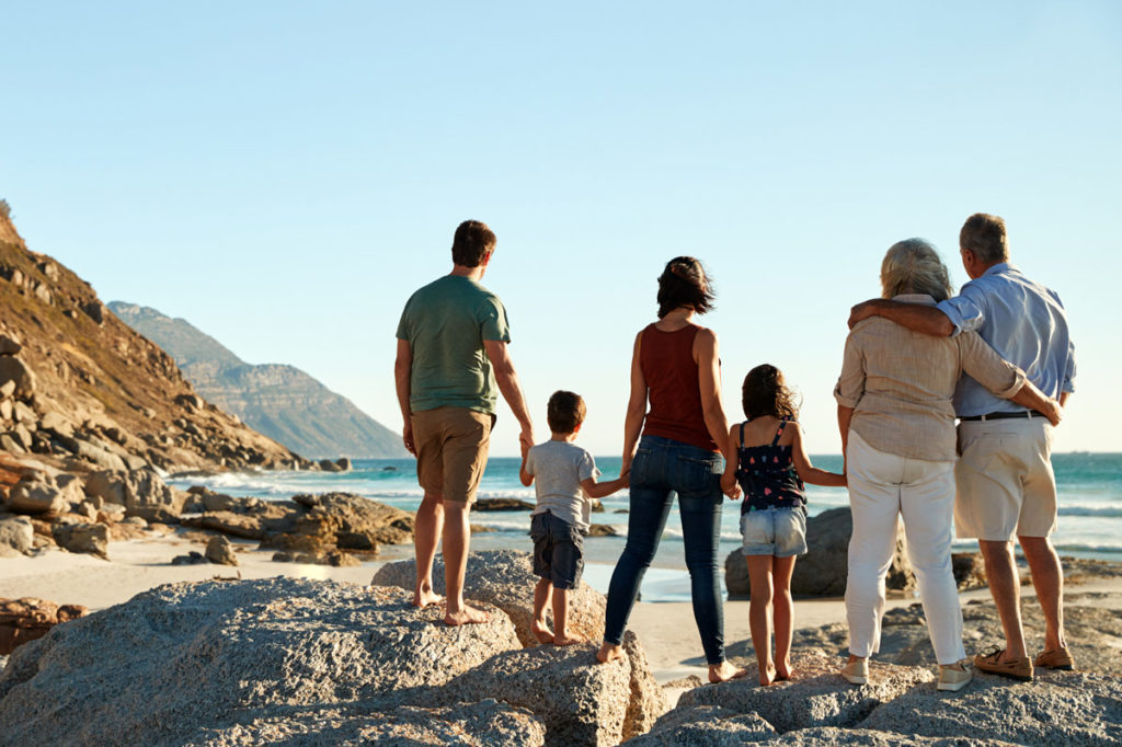Three generational family on a beach stand holding hands, admiring view.