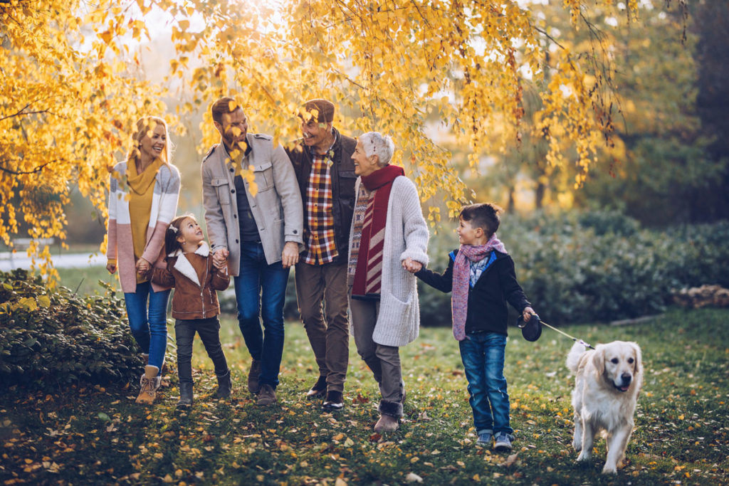 Happy extended family talking while taking a walk with their dog in autumn day in nature.